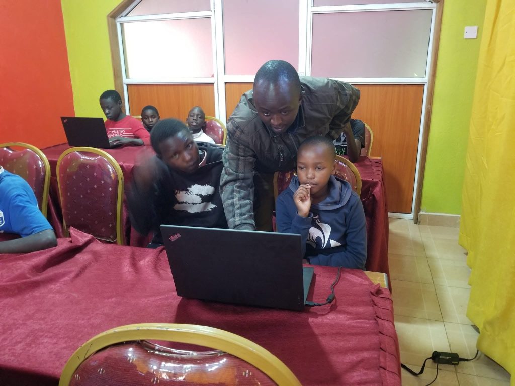 A mentor guiding a boy on a laptop